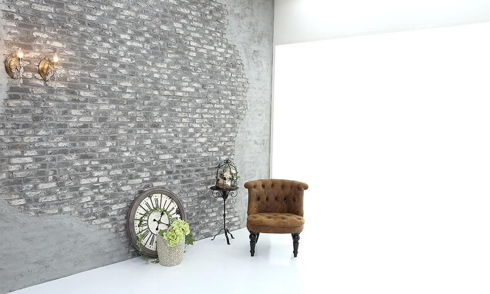 雰囲気のあるレンガの壁の前に、洋風な椅子や時計を配置したレトロな雰囲気の「マイブライド尾張旭」のスタジオイメージ