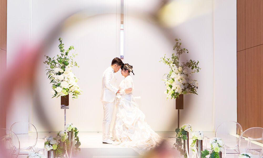 純白の「マイブライド津」のチャペルで向き合って洋装フォトを撮影する花嫁と新郎のイメージ