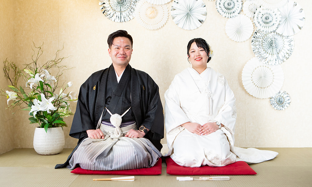 和の雰囲気のある傘や生け花の「マイブライド津」のスタジオで正座の和装フォトを撮影する花嫁と新郎のイメージ
