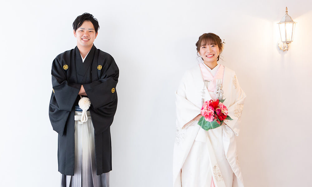 白の背景にアンティークなライトのある「マイブライド津」のスタジオで和装フォトを撮影する花嫁と新郎のイメージ